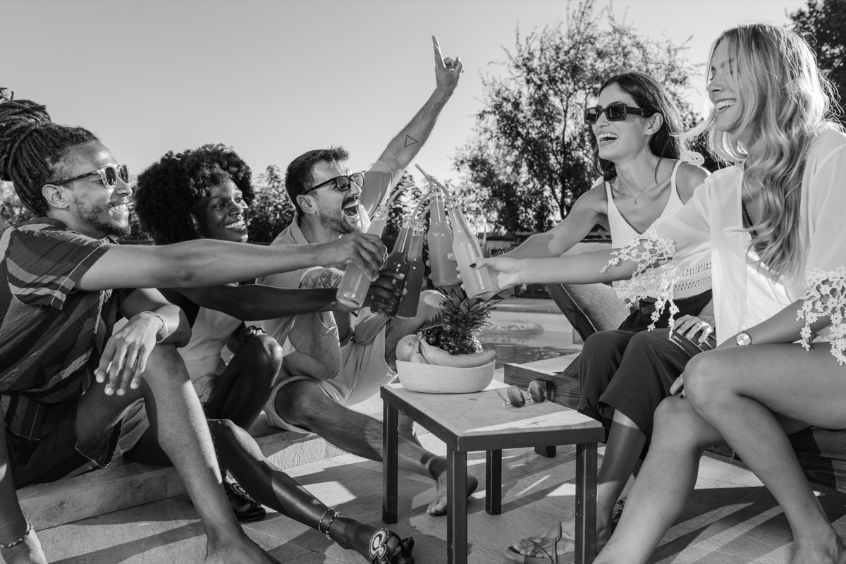 Friends clinking bottles around a low table in the afternoon sun.
